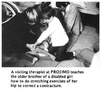 A visiting therapist at PROJIMO teaches the older brother of a disabled girl how to do stretching exercises of her hip to correct a contracture.