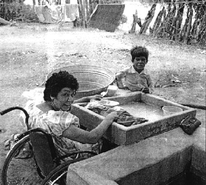 A mother, with her wheelchair, is washing clothes.